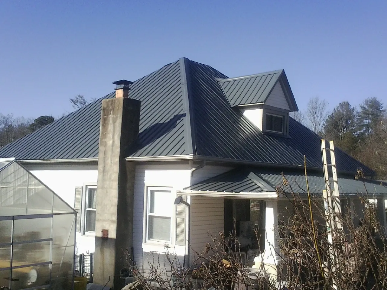 Dark blue standing seam metal roof on a white farmhouse with dormer — Slate & Tile Roof Repair by Roofing Brothers in Hinton