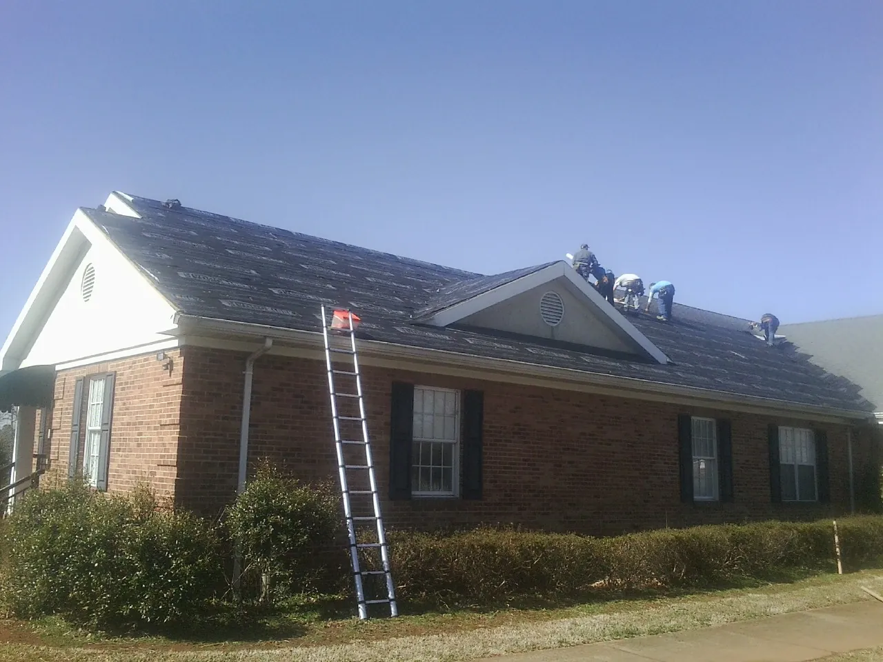 Crew tearing shingles off a brick ranch roof with a ladder set — Emergency Roof Repair work by our crew in Hinton