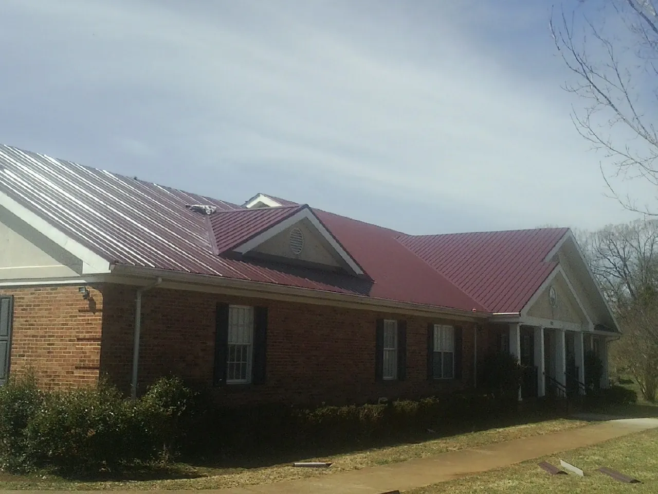 Red metal roof with gabled entries on a long brick building, from a Hail Damage Roof Repair job in Hinton