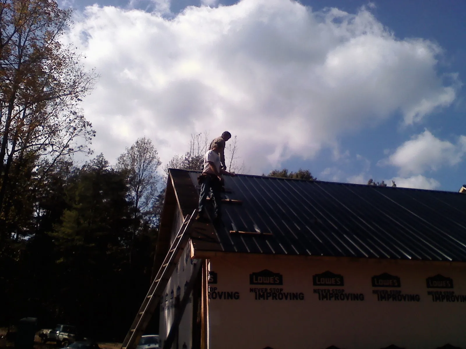 Roofer fastening dark metal panels high against a cloudy sky, from a Roof Inspection job in Hinton